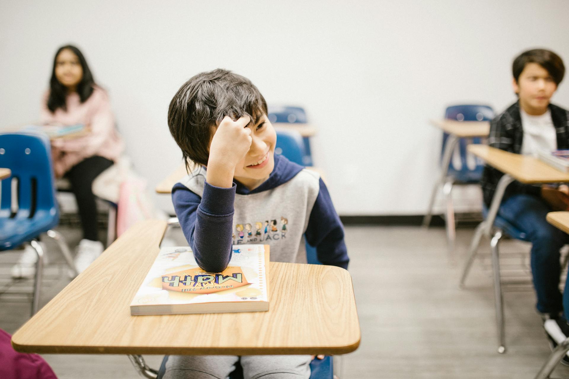 A smiling boy at his desk with a maths book in a classroom