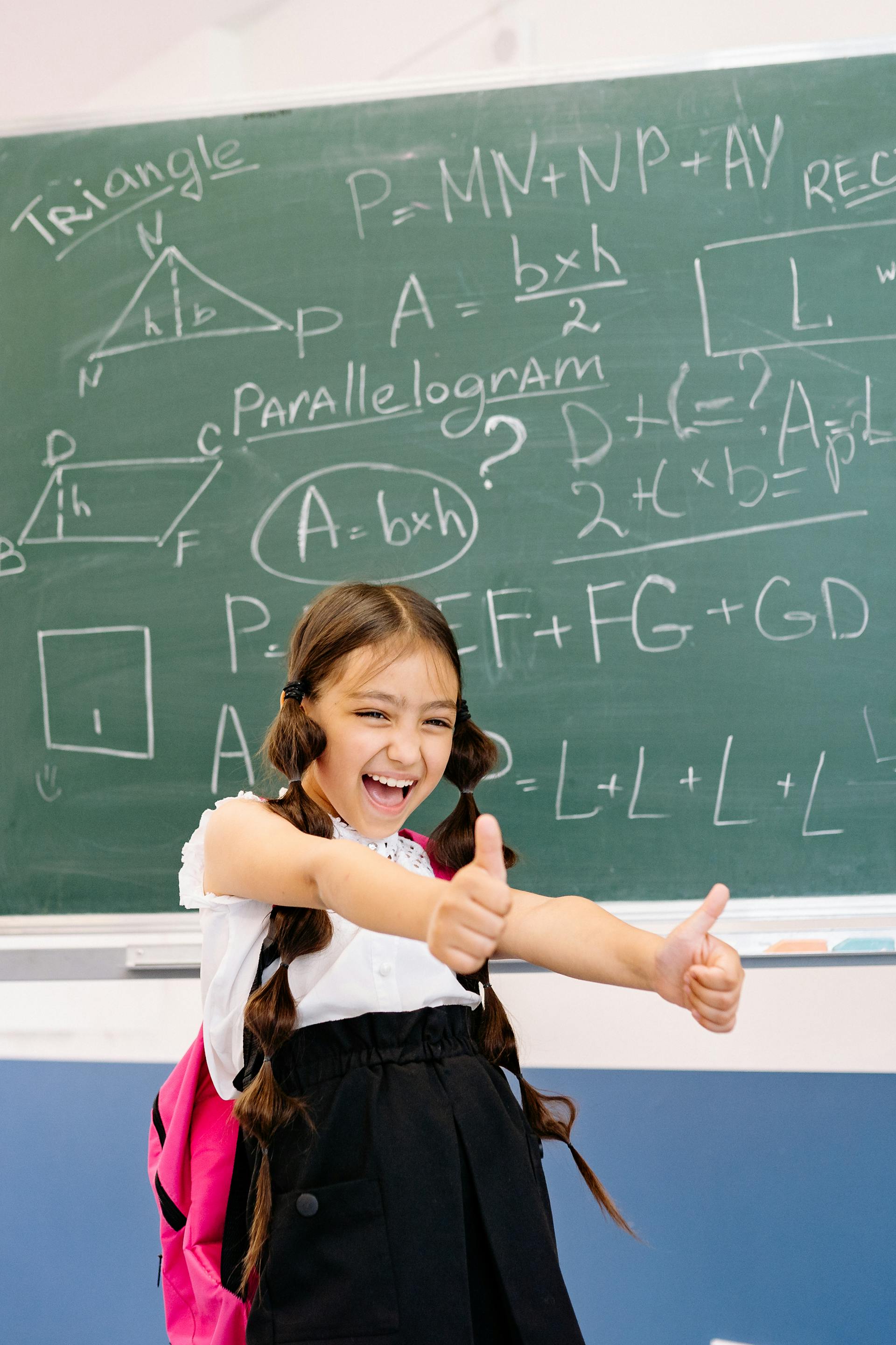 A girl giving thumbs up in front of a maths chalkboard