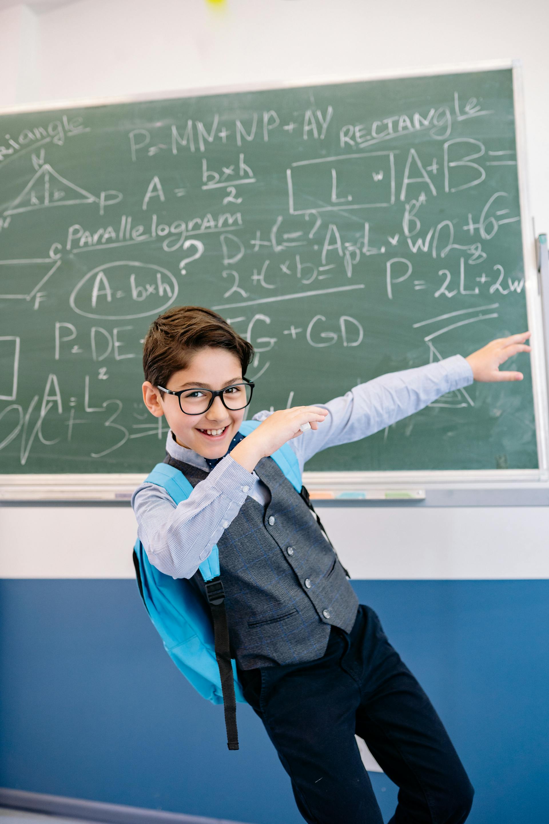 A boy in a waistcoat posing confidently by a maths chalkboard
