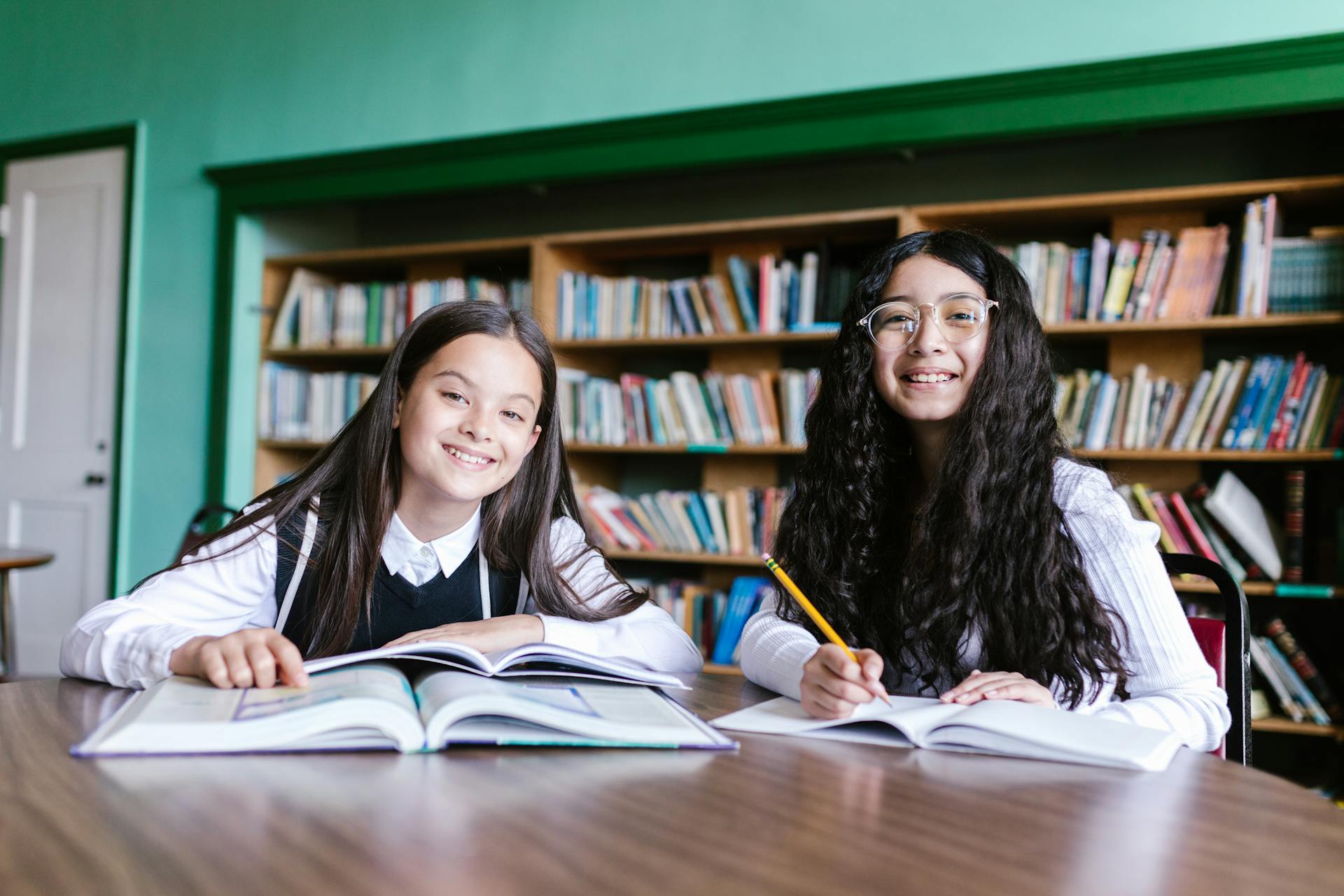 Two girls smiling while studying with books in a library