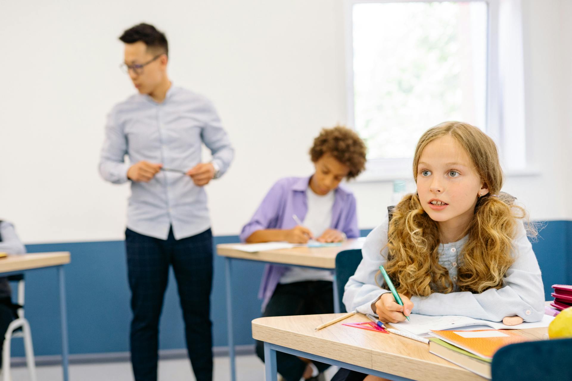 Students working at their desks with a tutor guiding them in a bright classroom